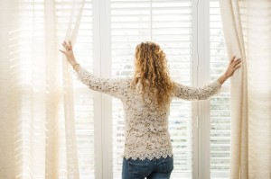 17592196 - woman looking out big bright window with curtains and blinds